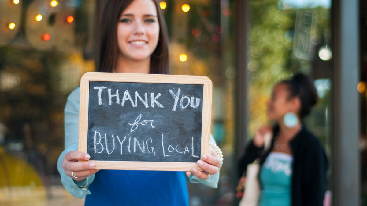 A woman holding a small chalk board that reads thank you for buying local